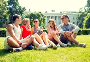 friendship, leisure, summer and people concept - group of smiling friends outdoors sitting and talking on grass on grass in park