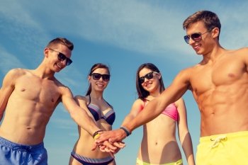 friendship, sea, holidays, gesture and people concept - group of smiling friends wearing swimwear and sunglasses putting hands on top of each other outdoors