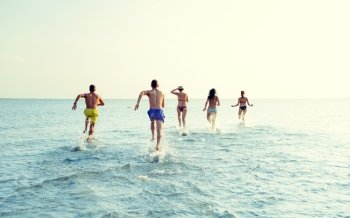 friendship, sea, summer vacation, holidays and people concept - group of smiling friends in swimwear running on beach from back