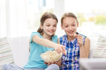 people, children, television, friends and friendship concept - two happy little girls watching tv and eating popcorn at home