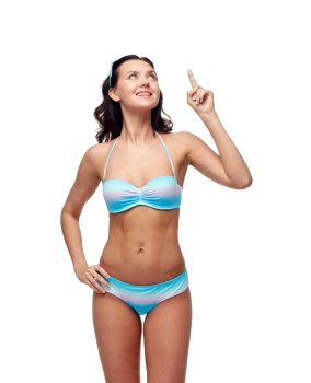 people, fashion, swimwear, summer and beach concept - happy young woman in bikini swimsuit pointing finger and looking up to something imaginary