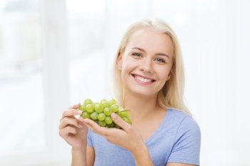 healthy eating, food, fruits, diet and people concept - happy woman eating grapes at home
