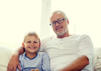 family, happiness, generation and people concept - smiling grandfather with grandson sitting on couch at home