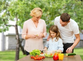 vegetarian food, culinary, happiness and people concept - happy family cooking vegetable salad for dinner over house and summer garden background