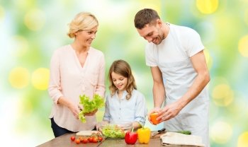 vegetarian food, culinary, happiness and people concept - happy family cooking vegetable salad for dinner in home kitchen green lights background