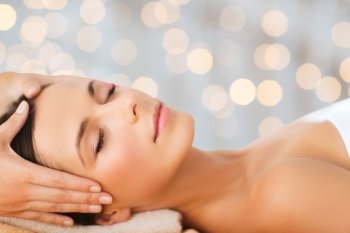 spa, beauty, people and body care concept - beautiful woman getting face treatment over holidays lights background