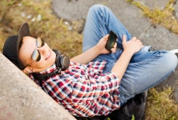 summer holidays, teenage and technology concept - teenager with headphones and smartphone outside