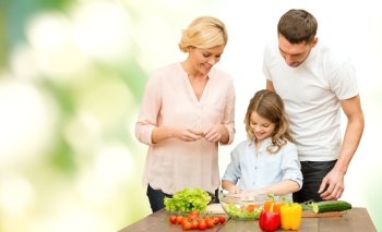 vegetarian food, culinary, happiness and people concept - happy family cooking vegetable salad for dinner over green natural background