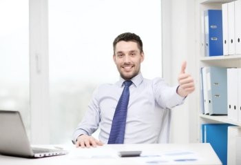 business, technology, finances and internet concept - smiling businessman with laptop computer and documents at office showing thumbs up