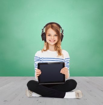 music, technology, people and childhood concept - happy girl with headphones showing tablet pc computer blank screen over green chalk board background