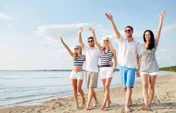 summer, holidays, sea, tourism and people concept - group of smiling friends in sunglasses walking on beach and waving hands