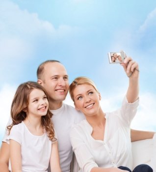 family, technology and people - smiling mother, father and little girl making selfie with camera over blue sky background