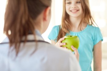 health care, healty eating, people, children and medicine concept - close up of doctor or stomatologist giving green apple to happy girl at hospital