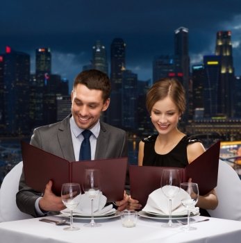 food, holidays and people concept - smiling couple with menus at restaurant over night city background