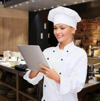 cooking, people, technology and food concept - smiling female chef, cook or baker with tablet pc computer over restaurant kitchen background