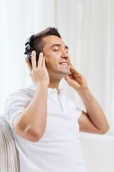technology, people and lifestyle concept - happy man in headphones listening to music at home