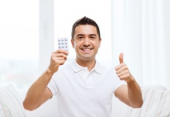 people, medication, medicine and health care concept - happy man showing thumbs up and holding pack of pills at home