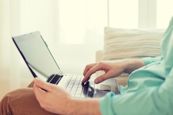 technology, home and lifestyle concept - close up of man working with laptop computer and sitting on sofa at home