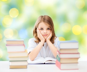 education, people, children and school concept - little student girl sitting at table with books over green lights background