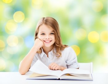 education, people, children and school concept - little student girl sitting at table with book over green lights background