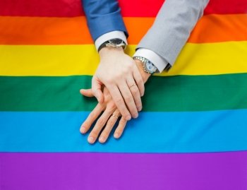 people, homosexuality, same-sex marriage, gay and love concept - close up of happy male gay couple hands over rainbow flag