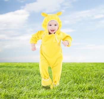 people, children, achievement and happiness concept - happy baby in yellow suit making first steps over blue sky and grass background