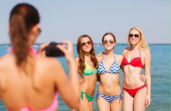 summer vacation, gesture, travel and people concept - group of smiling young women photographing by camera and waving hands on beach