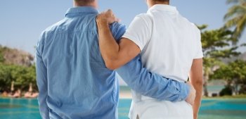people, same-sex marriage, honeymoon, travel and vacation concept - close up of happy male gay couple or friends hugging from back over exotic resort beach background