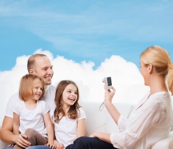 family, technology and people - smiling mother, father and little girls with camera over blue sky and white cloud background