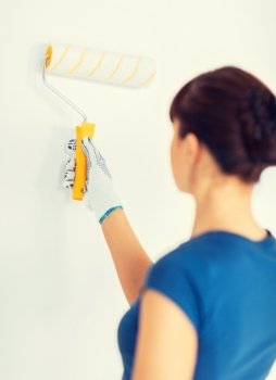 interior design and home renovation concept - woman with roller and paint colouring the wall. woman with roller and paint colouring the wall