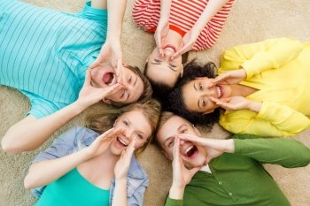 education and happiness concept - group of young smiling people lying down on floor in circle screaming and shouting. smiling people lying down on floor and screaming