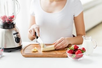 healthy eating, cooking, vegetarian food, dieting and people concept - close up of young woman with blender chopping banana for fruit shake at home