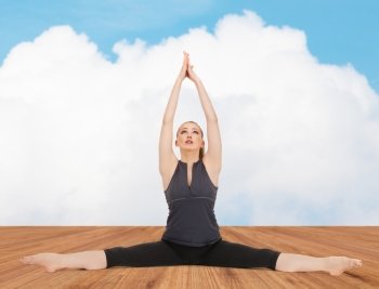people, health, wellness and sport concept - happy young woman in yoga pose on wooden floor over white cloud and blue sky background