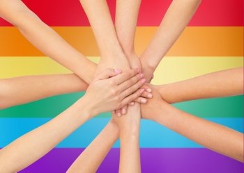 people, gesture, gay pride and homosexual concept - close up of women hands on top of each other over rainbow flag stripes background