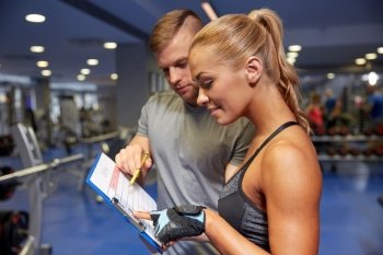 fitness, sport, exercising and diet concept - smiling young woman with personal trainer and exercise plan on clipboard in gym