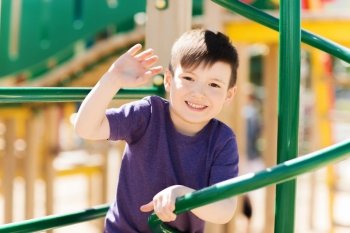 summer, childhood, leisure, gesture and people concept - happy little boy waving hand on children playground climbing frame