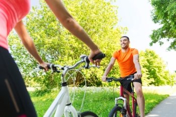 fitness, sport, people and healthy lifestyle concept - close up of happy couple riding bicycle outdoors at summer