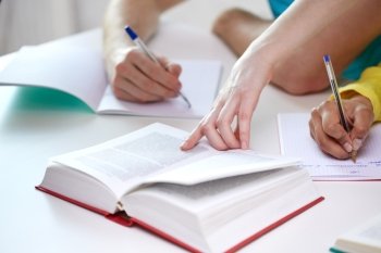 education, people and school concept - close up of students hands with textbooks writing to notebooks at school