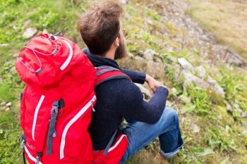 adventure, travel, tourism, hike and people concept - man hiker with red backpack sitting on ground