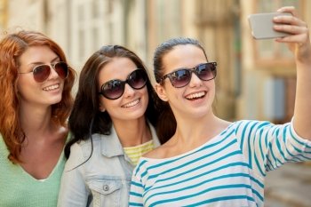 lifestyle, leisure, technology and people concept - smiling young women or teenage friends in sunglasses taking selfie with smartphone outdoors