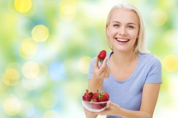 healthy eating, food, fruits, diet and people concept - happy woman eating strawberry over summer green holidays lights background