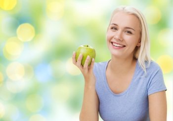 healthy eating, organic food, fruits, diet and people concept - happy woman eating green apple over summer green holidays lights background