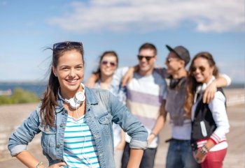 summer holidays and teenage concept - teenage girl in sunglasses and headphones hanging out with friends outside. teenage girl with headphones and friends outside