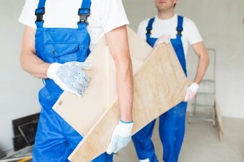 building, carpentry, repair, teamwork and people concept - close up of builders carrying wooden boards