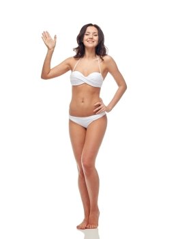 people, fashion, swimwear, summer and beach concept - happy young woman in white bikini swimsuit waving hand