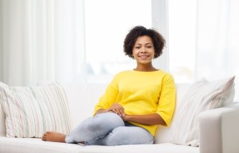 people, race, ethnicity and leisure concept - happy african american young woman sitting on sofa at home