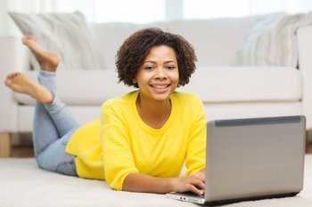 people, technology and leisure concept - happy african american young woman lying on floor with laptop computer at home