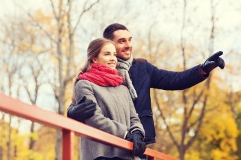 love, gesture, family, season and people concept - smiling couple hugging on bridge in autumn park