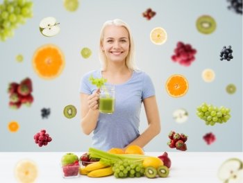 healthy eating, vegetarian food, diet, detox and people concept - smiling woman drinking green vegetable juice or shake from glass over fruits and berries on gray background