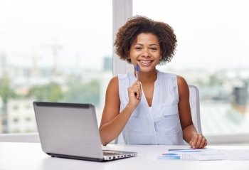 education, business and technology concept - happy african american businesswoman or student with laptop computer and papers at office
